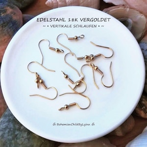 Könnte beinhalten: Eine Sammlung von ohrhaken aus goldfarbenem Metall mit einer kleinen Perle, angeordnet auf einer weißen runden Oberfläche. Der Text EDELSTAHL 18K VERGOLDET ~ • VERTIKALE SCHLAUFEN • ~ und BohemianChildByLyinn ist auf der weißen Oberfläche aufgedruckt.