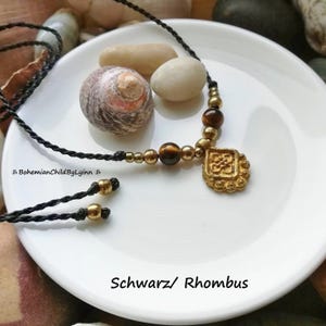 Könnte beinhalten: Eine schwarze Kordelkette mit goldfarbenen Perlen und einem quadratischen Anhänger. Der Anhänger hat ein dekoratives Design. Die Kette hat auch Tigeraugenperlen. Der Text auf dem Bild lautet "BohemianChildByLynn" und "Schwarz/ Rhombus".
