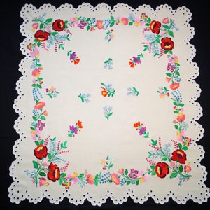 Puede incluir: Mantel blanco con borde festoneado y bordado floral en rojo, rosa, azul, verde y amarillo.