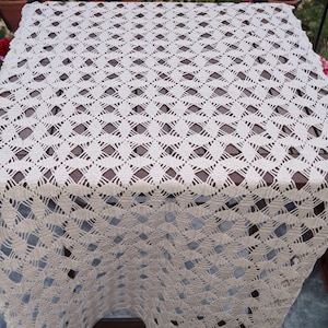 May include: A white crocheted tablecloth with a diamond pattern. The tablecloth is laid out on a wooden table.