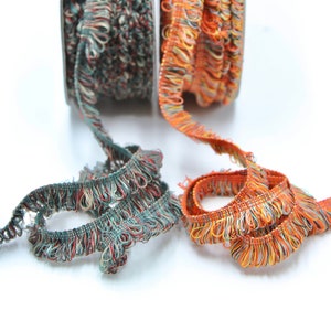 May include: Two spools of colorful trim with a fringed edge. One spool is teal and orange, the other is orange and yellow.