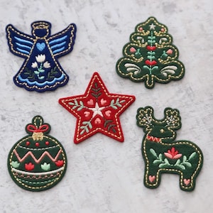 May include: Five embroidered Christmas decorations: a red star, a green Christmas tree, a green bauble, a green reindeer, and a blue angel.
