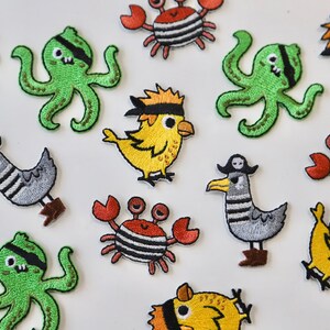 May include: A collection of colourful embroidered iron-on patches featuring various sea creatures, including crabs, octopuses, and birds. Each patch has a pirate theme with eye patches and bandanas.