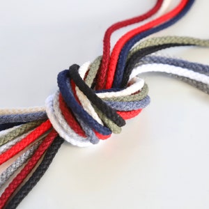 May include: A collection of colourful cotton cords tied together in a knot. The cords are in various shades of red, blue, green, white, and grey.