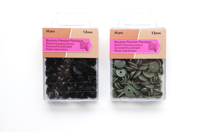 K&ouml;nnte beinhalten: Zwei Packungen mit je 30 schwarzen und gr&uuml;nen Kunststoff-Druckkn&ouml;pfen, jeweils 12 mm im Durchmesser. Die Packungen sind mit "Boutons Pression Plastique" und "MEDIAC" beschriftet.