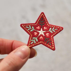 Peut inclure: Une &eacute;toile rouge en feutre avec des coutures dor&eacute;es et un motif brod&eacute; de feuilles et de fleurs blanches, roses et vertes.