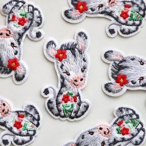 May include: A set of eight embroidered iron-on patches featuring a cute cartoon zebra with red flowers. The patches are perfect for adding a whimsical touch to clothing, bags, or other fabric items.