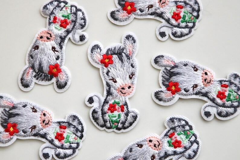 May include: A set of eight embroidered iron-on patches featuring a cute cartoon zebra with red flowers. The patches are perfect for adding a whimsical touch to clothing, bags, or other fabric items.