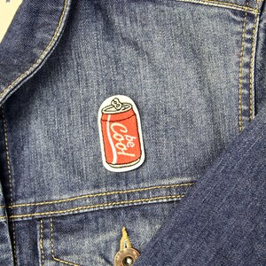 May include: A denim jacket with a red and white embroidered patch of a soda can that says "Be Cool" on it.