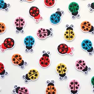 May include: Assortment of colourful embroidered ladybug patches with black spots. The patches are various colours including red, orange, yellow, green, blue, and pink.