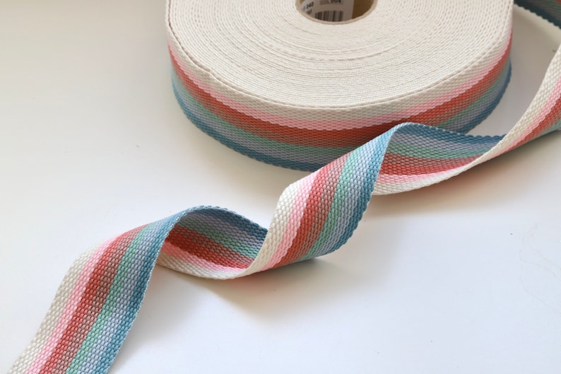 May include: A roll of white cotton webbing with pink, green, and blue stripes. The webbing is 1 inch wide.