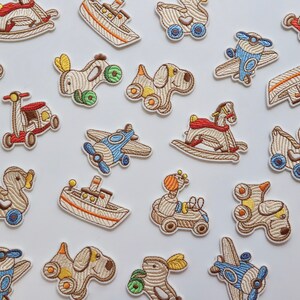 May include: A collection of embroidered iron-on patches featuring various whimsical designs, including a rocking horse, a duck, a plane, a boat, a scooter, and a dog. The patches are made of beige fabric with colourful details.