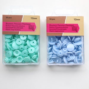 K&ouml;nnte beinhalten: Zwei Packungen mit je 30 Kunststoff-Druckkn&ouml;pfen, eine in hellblau und eine in hellgr&uuml;n. Jede Packung ist mit "30 Stk" und "12 mm" beschriftet und tr&auml;gt den Markennamen "MEDIAC".
