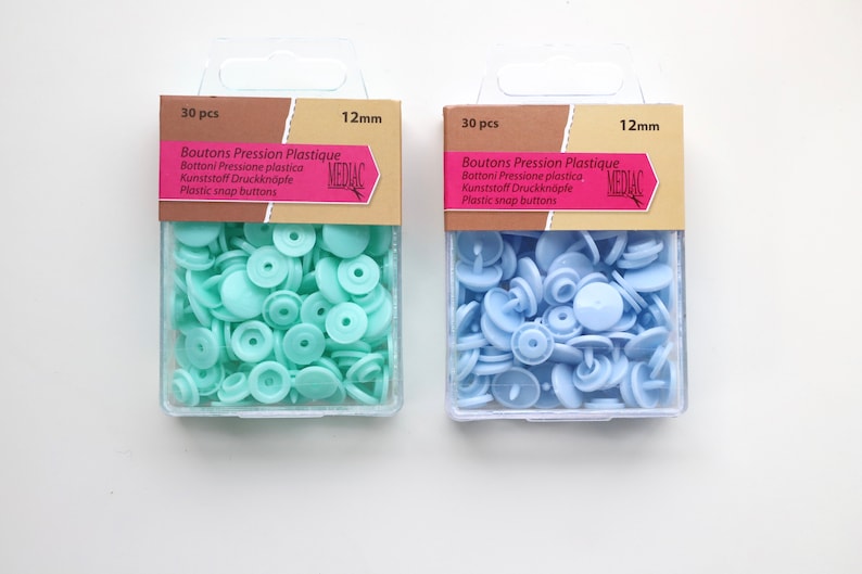 K&ouml;nnte beinhalten: Zwei Packungen mit je 30 Kunststoff-Druckkn&ouml;pfen, eine in hellblau und eine in hellgr&uuml;n. Jede Packung ist mit "30 Stk" und "12 mm" beschriftet und tr&auml;gt den Markennamen "MEDIAC".