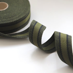 May include: A roll of green and black striped webbing ribbon. The ribbon is woven with a textured pattern.