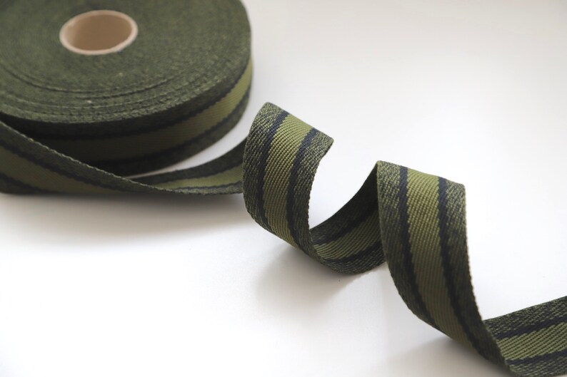 May include: A roll of green and black striped webbing ribbon. The ribbon is woven with a textured pattern.