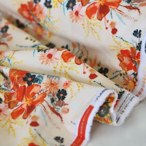 Peut inclure: Gros plan sur un tissu blanc à imprimé floral avec des fleurs rouges, orange, jaunes et bleues. Le tissu est plié et possède une bordure blanche avec des coutures rouges. Le tissu est étiqueté "40" et "Sewn with TRIBUTO" en texte noir.