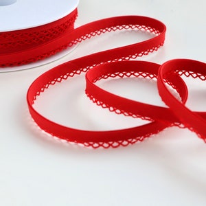 May include: Red elastic trim with a decorative lace edge. The trim is wound around a white spool.
