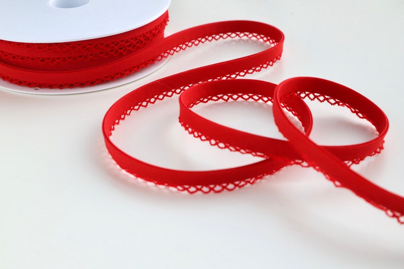 May include: Red elastic trim with a decorative lace edge. The trim is wound around a white spool.