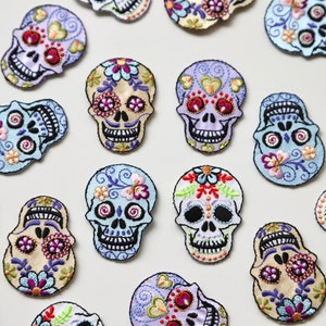 May include: A collection of 15 colourful embroidered sugar skull patches. The skulls are decorated with flowers, hearts, and swirls. The patches are perfect for adding a touch of whimsy to clothing, bags, or other accessories.