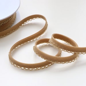 May include: A spool of brown velvet ribbon with a gold lace trim. The ribbon is rolled up on a white spool.
