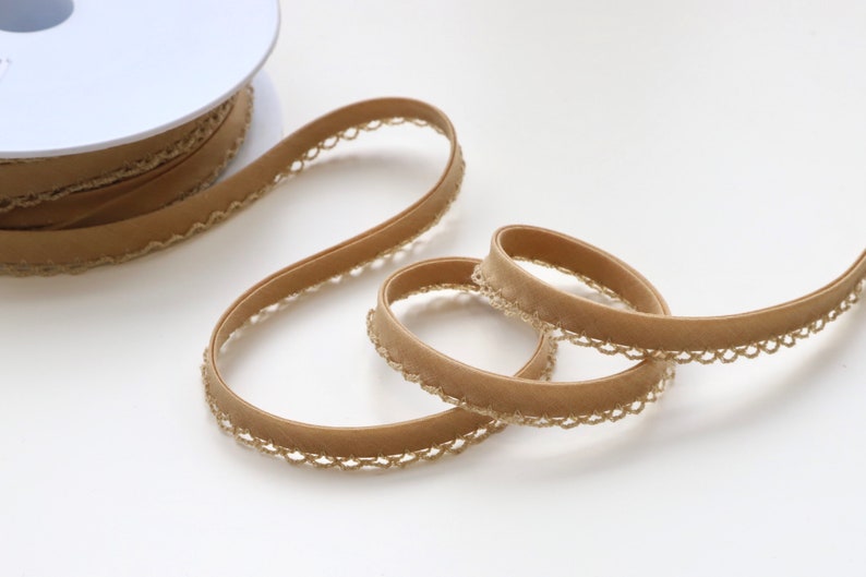May include: A spool of brown velvet ribbon with a gold lace trim. The ribbon is rolled up on a white spool.