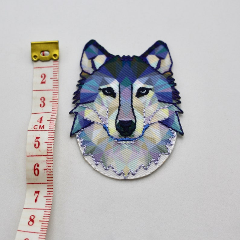 May include: A blue and white geometric wolf head iron-on patch. The patch is approximately 5 cm in diameter.