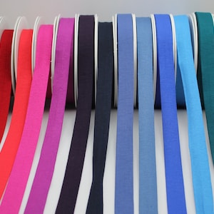 May include: Assortment of 14 spools of cotton ribbon in various colours, including red, orange, pink, purple, blue, green, and yellow. The ribbon is approximately 2.5 cm wide.