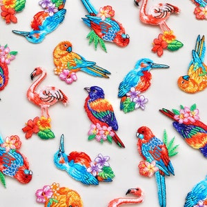 May include: A collection of colourful embroidered iron-on patches featuring tropical birds and flowers. The patches include flamingos, parrots, and other birds with vibrant colours like blue, red, orange, and yellow.