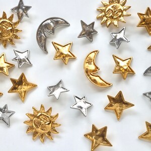 Puede incluir: Una colecci&oacute;n de abalorios de metal dorado y plateado con estrellas, lunas y soles. Los abalorios tienen un acabado texturizado y martillado.
