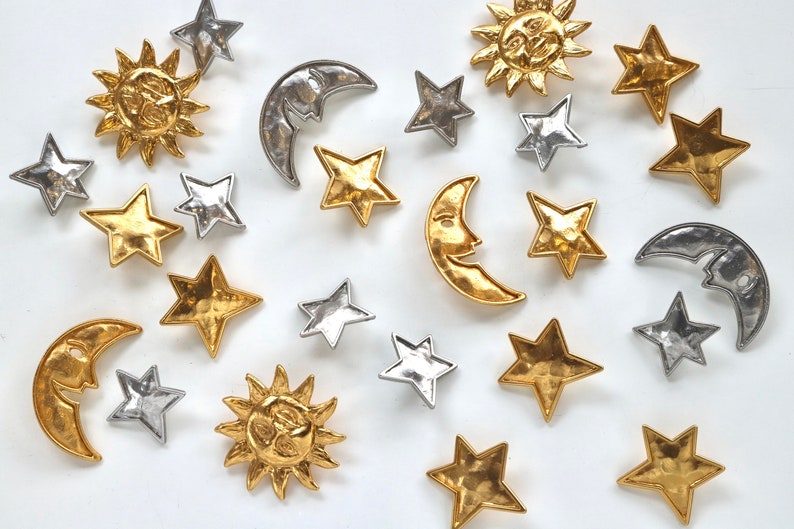 Puede incluir: Una colecci&oacute;n de abalorios de metal dorado y plateado con estrellas, lunas y soles. Los abalorios tienen un acabado texturizado y martillado.