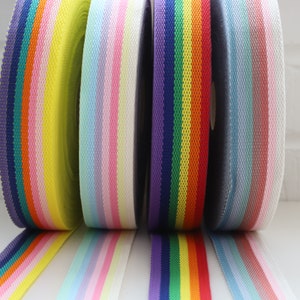 May include: Five rolls of colorful striped ribbon. The ribbons are in shades of yellow, pink, purple, blue, and gray.