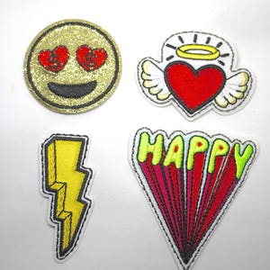 May include: Four embroidered iron-on patches. One is a gold glitter smiley face with red hearts for eyes. Another is a red heart with white wings and a halo. The third is a yellow lightning bolt. The last is a red and green word patch that says "HAPPY".