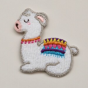 Puede incluir: Parche de llama blanco bordado con un dise&ntilde;o de manta de silla de montar colorida. La llama tiene los ojos cerrados y la nariz rosa.