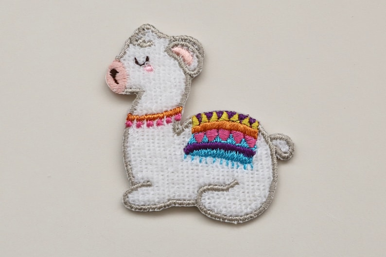 Puede incluir: Parche de llama blanco bordado con un dise&ntilde;o de manta de silla de montar colorida. La llama tiene los ojos cerrados y la nariz rosa.
