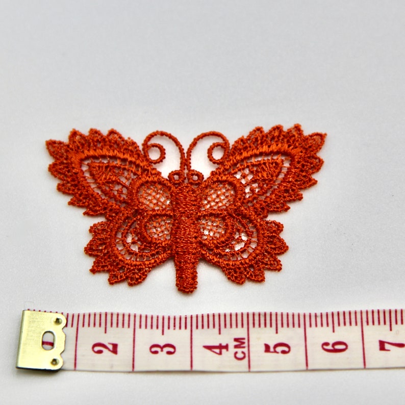 May include: A rust-colored lace butterfly applique measuring approximately 4 cm wide. The butterfly has intricate details and a delicate design.