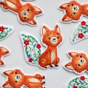 May include: A set of nine embroidered iron-on patches featuring foxes with floral details. The foxes are orange and brown with white accents. The flowers are red, blue, and green.