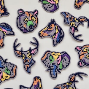 May include: A set of 13 colourful embroidered iron-on patches featuring various animals, including a bear, deer, horse, elephant, and a few others. The patches are all in a similar style, with a grey background and colourful embroidery.