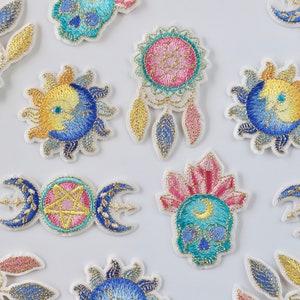 May include: Assortment of embroidered iron-on patches featuring celestial and mystical designs. The patches include a sun and moon, a dream catcher, a skull with a crescent moon, and a triple moon with a pentagram.