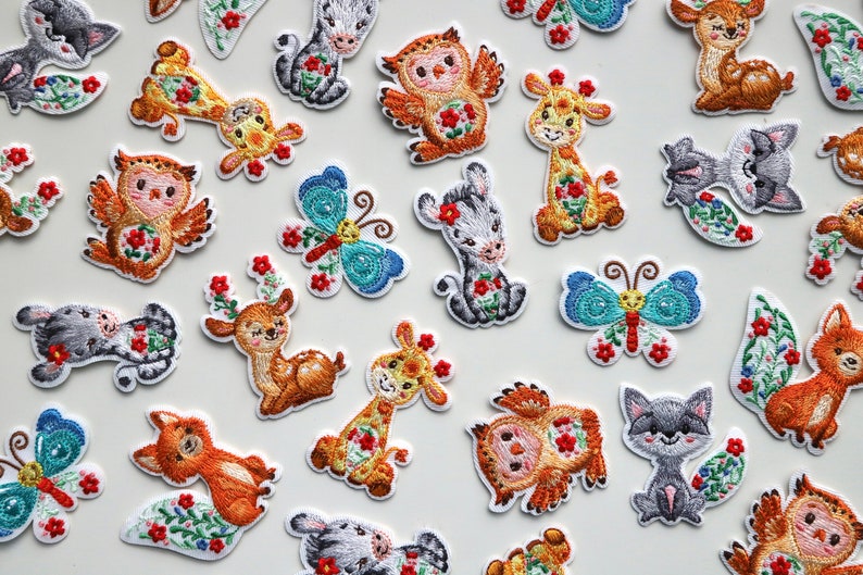 May include: A collection of embroidered iron-on patches featuring various animals and insects. The patches are colorful and feature a variety of designs, including a deer, a fox, an owl, a butterfly, and a giraffe. The patches are perfect for adding a touch of whimsy to clothing, bags, or other fabric items.
