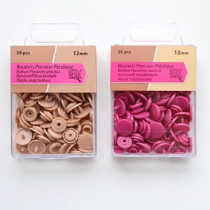 K&ouml;nnte beinhalten: Zwei Packungen mit je 30 Kunststoff-Druckkn&ouml;pfen, jeweils 12 mm gro&szlig;. Eine Packung enth&auml;lt beige Kn&ouml;pfe, die andere enth&auml;lt rosa Kn&ouml;pfe. Die Packungen sind mit "Boutons Pression Plastique" und "MEDIAC" beschriftet.