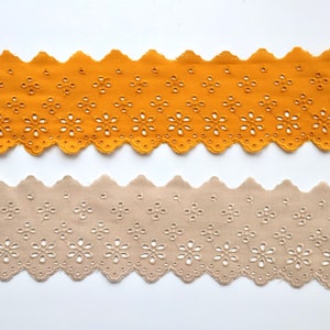 May include: Two pieces of scalloped cotton lace trim with a floral pattern. The top piece is mustard yellow and the bottom piece is beige.
