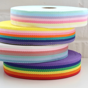 May include: Four rolls of colorful striped ribbon, stacked on top of each other. The ribbon is made of a woven fabric and has a variety of colors, including pink, blue, yellow, green, and red.