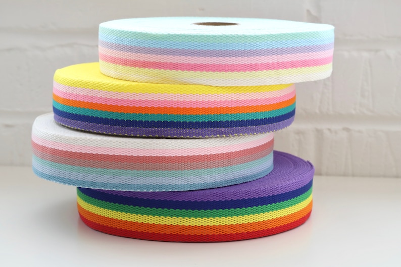 May include: Four rolls of colorful striped ribbon, stacked on top of each other. The ribbon is made of a woven fabric and has a variety of colors, including pink, blue, yellow, green, and red.