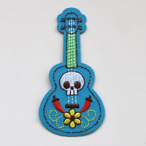 May include: A blue embroidered guitar with a skull and flower design. The guitar has a green neck and red chilli peppers on the body.