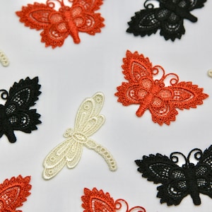 May include: Assortment of lace appliques in the shapes of butterflies and dragonflies. The butterflies are in black, orange, and white. The dragonflies are in white.