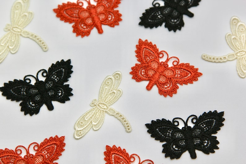 May include: Assortment of lace appliques in the shapes of butterflies and dragonflies. The butterflies are in black, orange, and white. The dragonflies are in white.