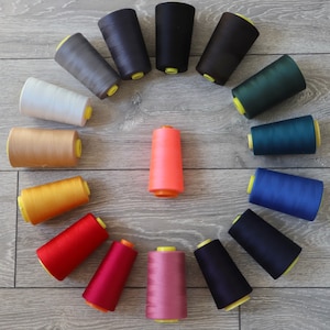 May include: A collection of 15 spools of thread in various colours, including red, blue, green, yellow, orange, pink, and grey. The spools are arranged in a circle on a wooden surface.