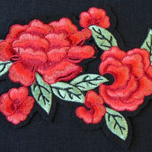 May include: Red embroidered flower patch with green leaves. The patch is made of fabric and has a stitched design.