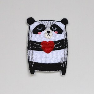 May include: Embroidered iron-on patch featuring a black and white panda holding a red heart. The panda has a cute, cartoon-like expression.